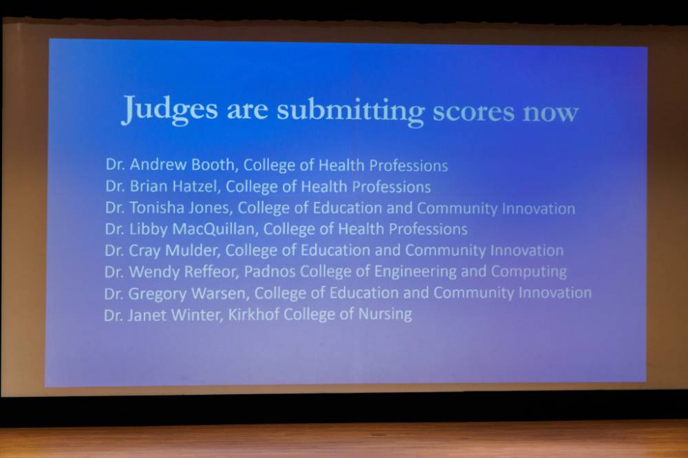 Presentation slide stating the 3MT judges are submitting their scores.